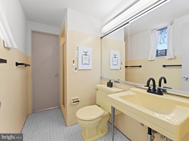full bath featuring tile walls, tile patterned flooring, a shower stall, a sink, and toilet