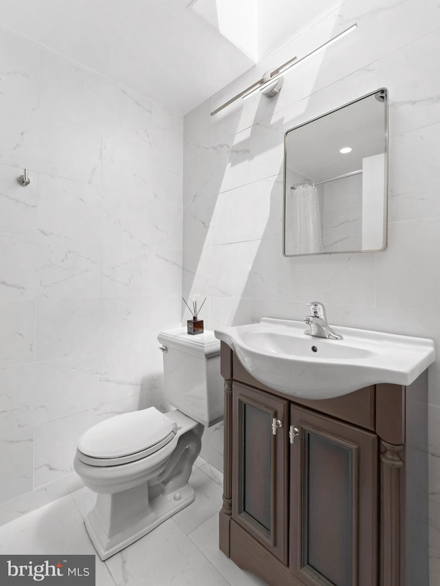 bathroom featuring tile walls, vanity, toilet, and marble finish floor