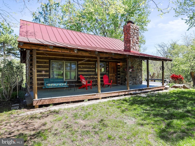 back of house featuring metal roof, a yard, a chimney, and a standing seam roof
