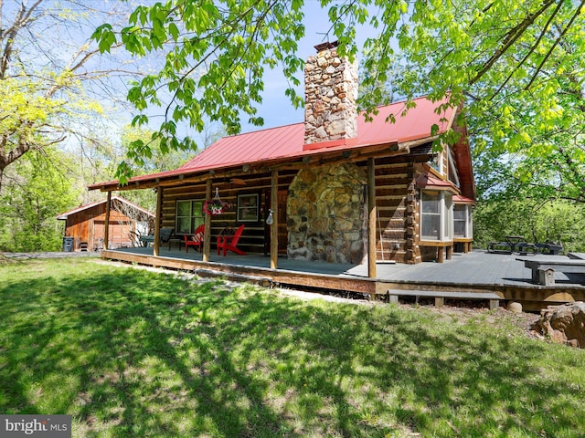 back of property featuring a chimney, metal roof, a wooden deck, a yard, and stone siding