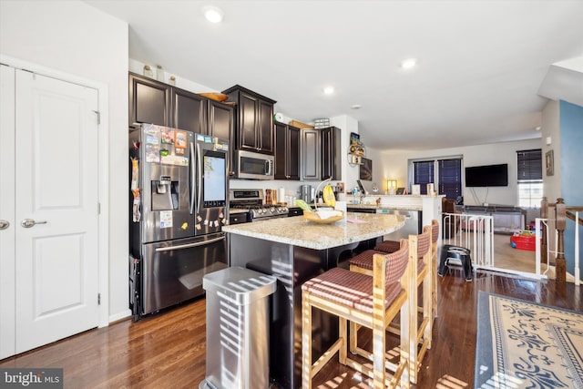 kitchen with appliances with stainless steel finishes, light stone countertops, dark wood-style floors, and a center island
