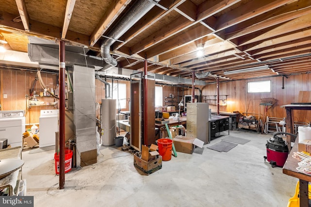 basement with washer and clothes dryer, water heater, and wood walls