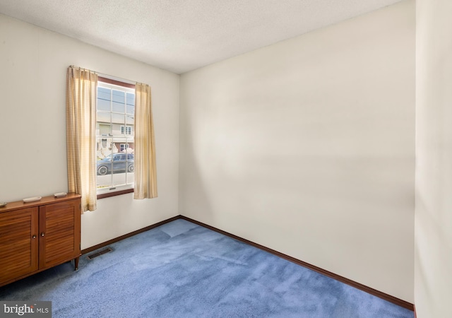 carpeted empty room with baseboards, a textured ceiling, and visible vents