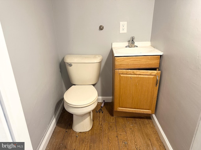 half bath featuring baseboards, wood finished floors, toilet, and vanity