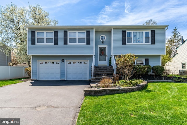 raised ranch with a front lawn, driveway, an attached garage, and fence