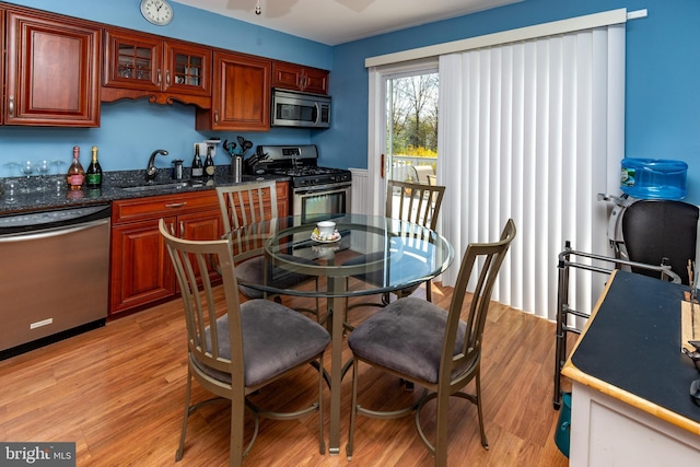 kitchen with a sink, stainless steel appliances, glass insert cabinets, light wood-type flooring, and a ceiling fan