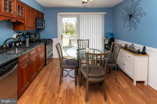 kitchen featuring light wood-type flooring, stainless steel appliances, a wainscoted wall, and a sink