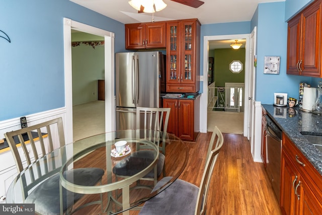 interior space with dark stone countertops, glass insert cabinets, stainless steel appliances, wood finished floors, and a ceiling fan