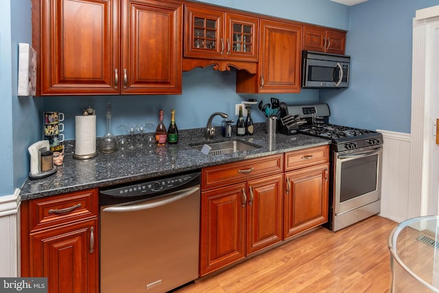 kitchen with dark stone countertops, a sink, light wood-style floors, stainless steel appliances, and a wainscoted wall