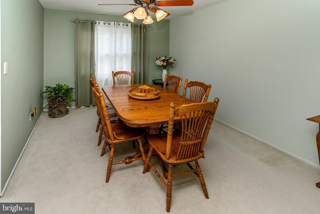 dining area with a ceiling fan, light colored carpet, and baseboards