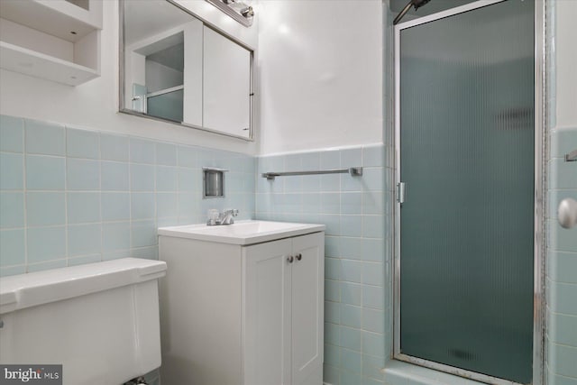 full bathroom featuring vanity, toilet, tile walls, a wainscoted wall, and a shower stall