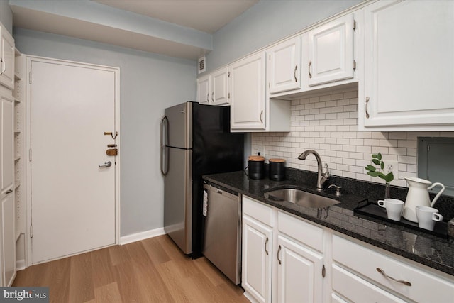 kitchen with white cabinets, appliances with stainless steel finishes, tasteful backsplash, a sink, and light wood-type flooring