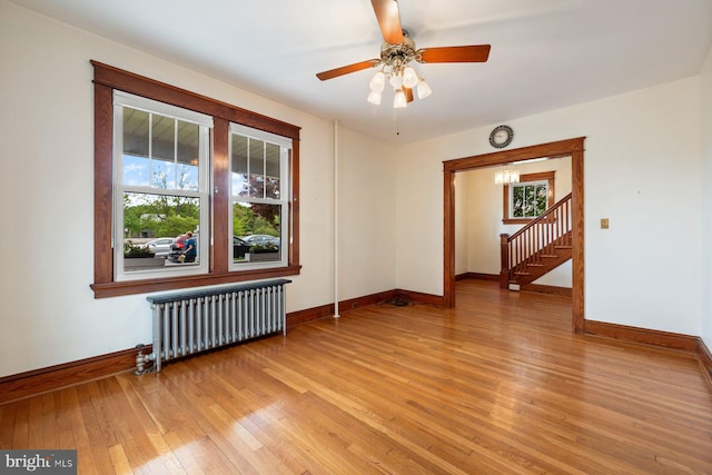 spare room featuring radiator heating unit, baseboards, ceiling fan with notable chandelier, and light wood-style flooring