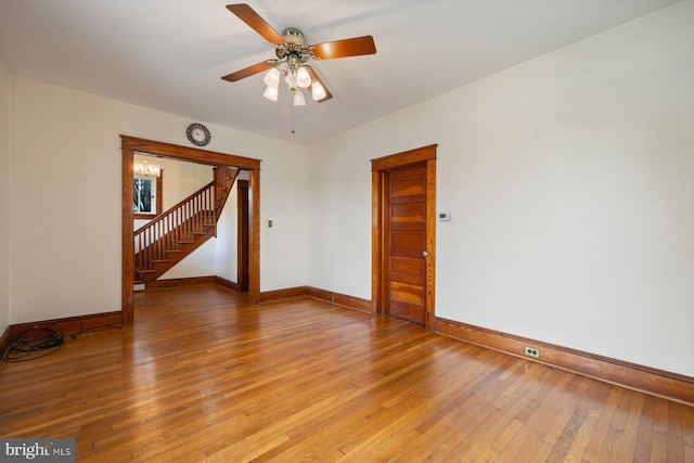 empty room with baseboards, ceiling fan, light wood-style flooring, and stairway