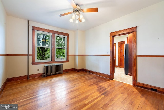 spare room with radiator, ceiling fan, baseboards, and light wood finished floors