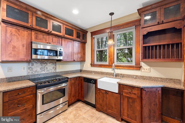 kitchen with appliances with stainless steel finishes, hanging light fixtures, light stone countertops, a sink, and light tile patterned flooring
