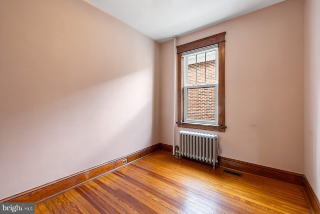 empty room with baseboards, visible vents, radiator heating unit, and hardwood / wood-style flooring