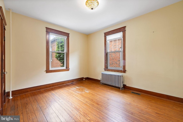 spare room featuring radiator, baseboards, wood-type flooring, and visible vents