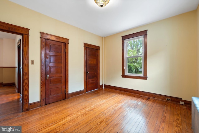 unfurnished bedroom featuring light wood-style floors, baseboards, and radiator heating unit