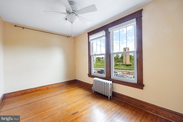 spare room featuring a ceiling fan, baseboards, radiator heating unit, and light wood-type flooring