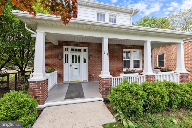 entrance to property with a porch, fence, and brick siding
