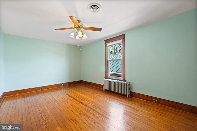 empty room featuring visible vents, baseboards, radiator heating unit, and hardwood / wood-style floors