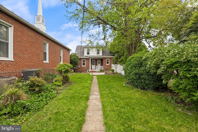 rear view of property featuring fence, a lawn, central AC, and brick siding