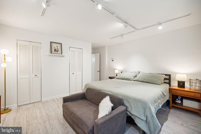 bedroom with light wood-style floors, baseboards, rail lighting, and two closets