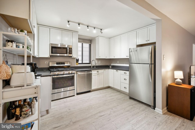 kitchen featuring a sink, light wood-type flooring, dark countertops, white cabinets, and appliances with stainless steel finishes