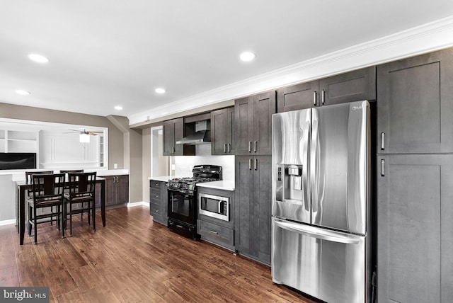 kitchen featuring stainless steel appliances, wall chimney range hood, ceiling fan, light countertops, and dark wood-style floors