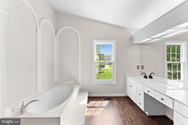 full bathroom with vanity, a garden tub, wood finished floors, vaulted ceiling, and baseboards