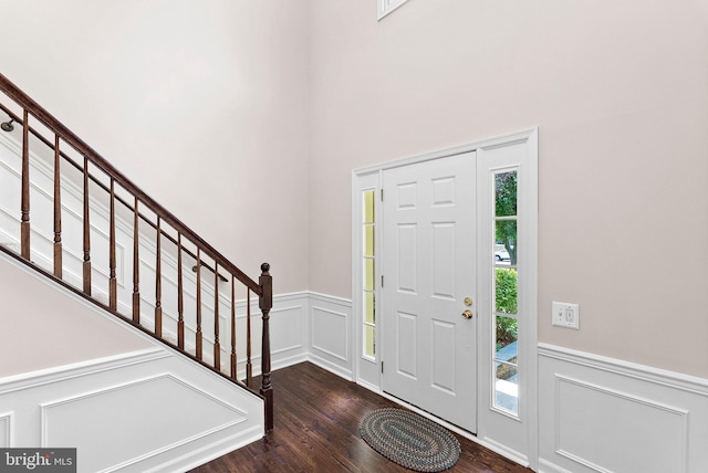 foyer entrance featuring wood finished floors, a wainscoted wall, stairway, a decorative wall, and a towering ceiling