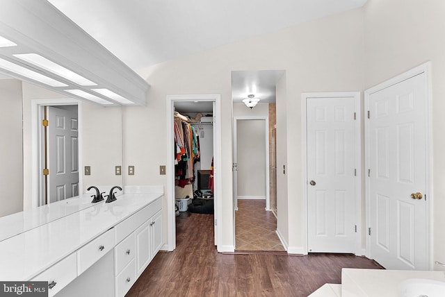 full bathroom featuring vanity, wood finished floors, lofted ceiling, a spacious closet, and baseboards