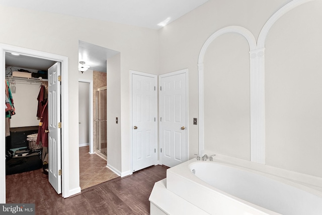 bathroom featuring wood finished floors, a shower stall, a garden tub, a walk in closet, and baseboards