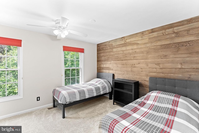 carpeted bedroom with wood walls, multiple windows, baseboards, and ceiling fan