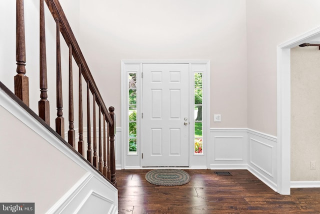 entrance foyer featuring healthy amount of natural light, dark wood-style flooring, stairs, a towering ceiling, and a wainscoted wall
