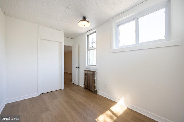 unfurnished bedroom featuring radiator heating unit, light wood-style floors, and baseboards