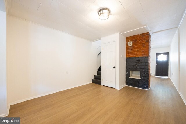 unfurnished living room featuring wood finished floors, a baseboard radiator, a large fireplace, baseboards, and stairway