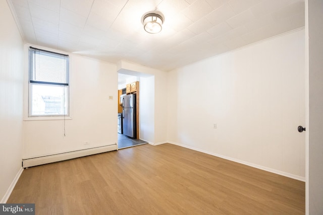 spare room with baseboards, wood finished floors, and a baseboard radiator