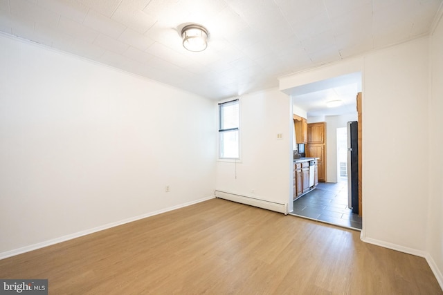 unfurnished room with a baseboard heating unit, light wood finished floors, and baseboards