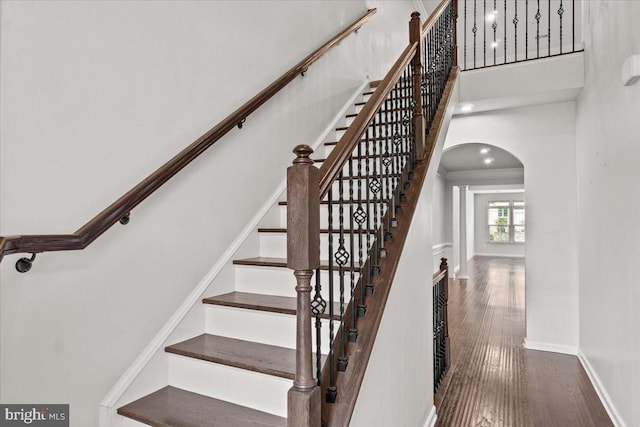 stairway featuring arched walkways, baseboards, wood finished floors, a towering ceiling, and ornamental molding