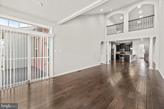 unfurnished living room with arched walkways, baseboards, dark wood finished floors, and a towering ceiling