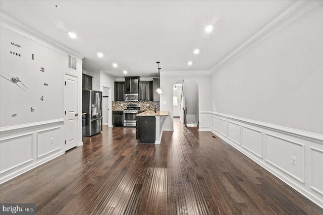 kitchen featuring crown molding, light countertops, arched walkways, dark cabinetry, and stainless steel appliances