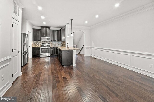 kitchen with appliances with stainless steel finishes, arched walkways, dark cabinets, a peninsula, and decorative backsplash