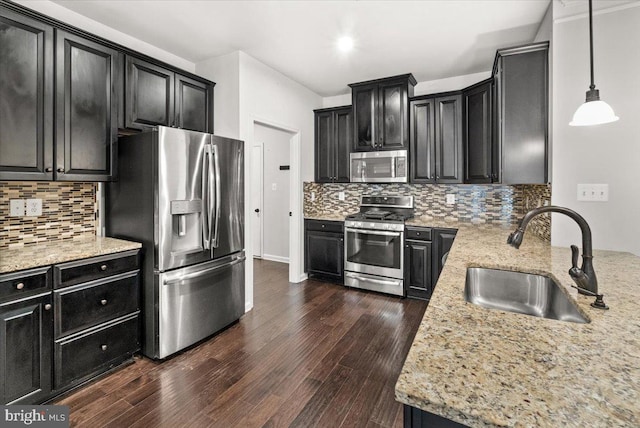 kitchen with decorative backsplash, dark wood-type flooring, dark cabinetry, a sink, and stainless steel appliances