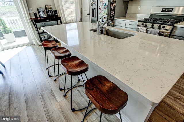 kitchen featuring light stone countertops, a sink, a kitchen bar, light wood-type flooring, and appliances with stainless steel finishes