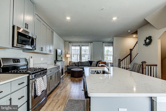 kitchen featuring a sink, stainless steel appliances, gray cabinets, light wood-type flooring, and open floor plan