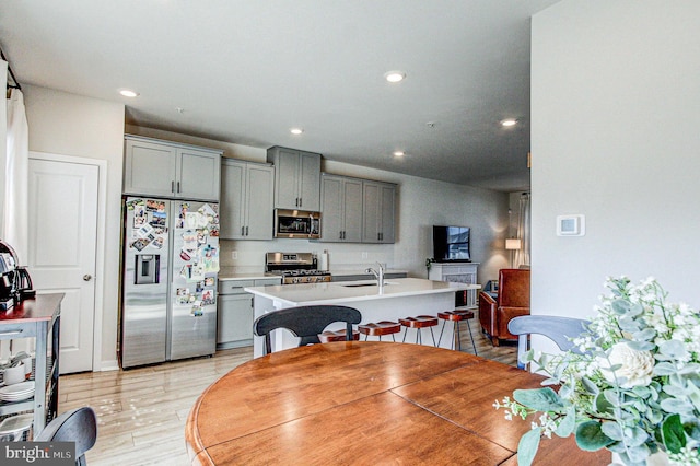kitchen featuring recessed lighting, a kitchen island with sink, stainless steel appliances, light countertops, and gray cabinetry