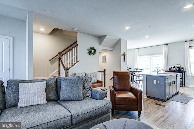 living room featuring light wood finished floors, recessed lighting, and stairs
