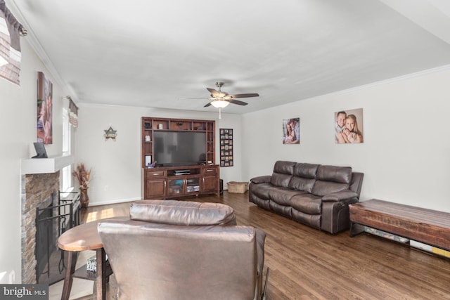 living room with wood finished floors, ceiling fan, ornamental molding, and a stone fireplace